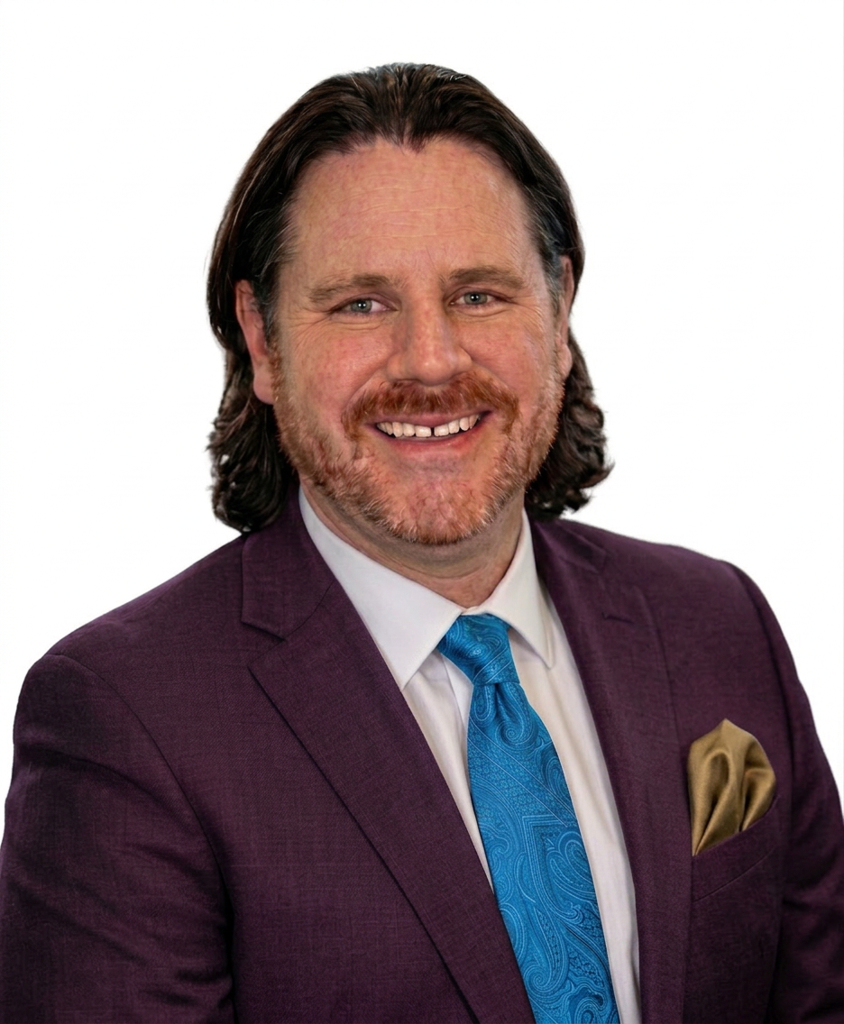 Smiling man wearing a purple suit, white shirt, and blue patterned tie with a gold pocket square